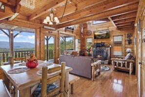 Interior de una cabaña de madera con chimenea, mobiliario rústico y una vista panorámica.