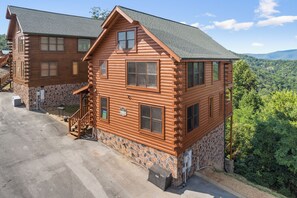 A two-story log cabin with a stone foundation, multiple windows, and a staircase leading to the upper level. - Luxurious Cabin|Majestic Views|Arcade|Hot Tub (Sevierville)