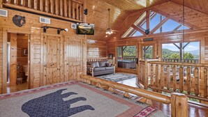 A wooden cabin interior with a large bed, a sofa, and a television mounted on the wall. - Luxurious Cabin|Majestic Views|Arcade|Hot Tub (Sevierville)