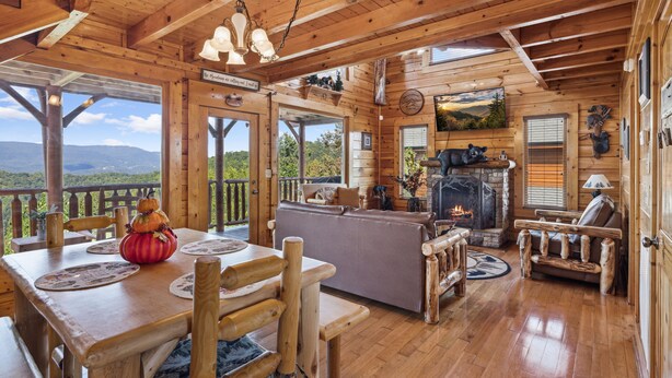 A wooden cabin interior with a dining area, sofa, fireplace, and large windows offering scenic views. - Luxurious Cabin|Majestic Views|Arcade|Hot Tub (Sevierville)