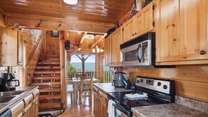 A wooden cabin kitchen with a stove, microwave, and wooden cabinets. - Luxurious Cabin|Majestic Views|Arcade|Hot Tub (Sevierville)