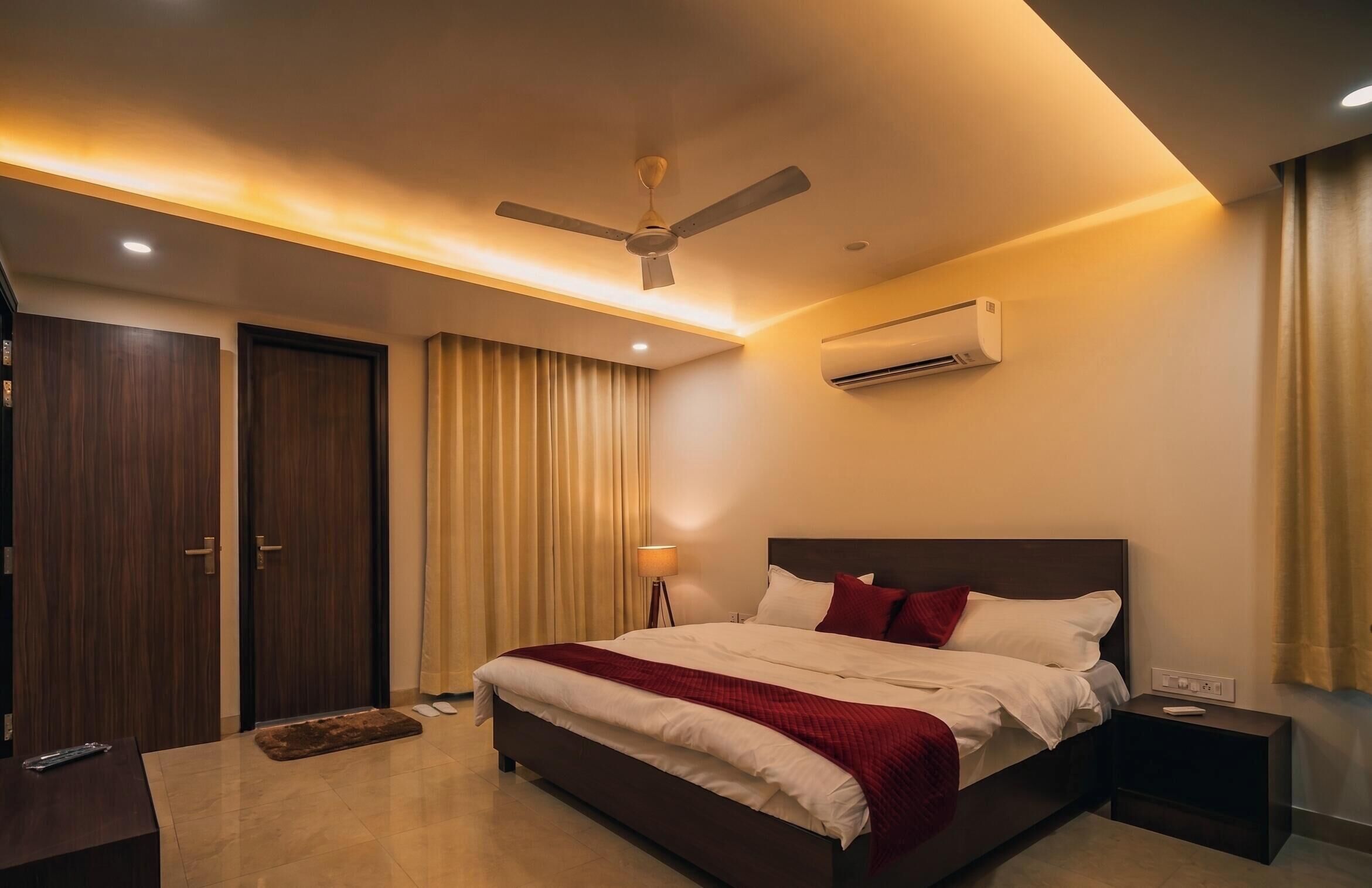 A hotel room with a bed, a ceiling fan, an air conditioning unit, a bedside table, and a nightstand.