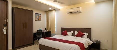 Habitación de hotel con cama, escritorio, aire acondicionado, ventilador de techo y puerta con cerradura de llave electrónica.