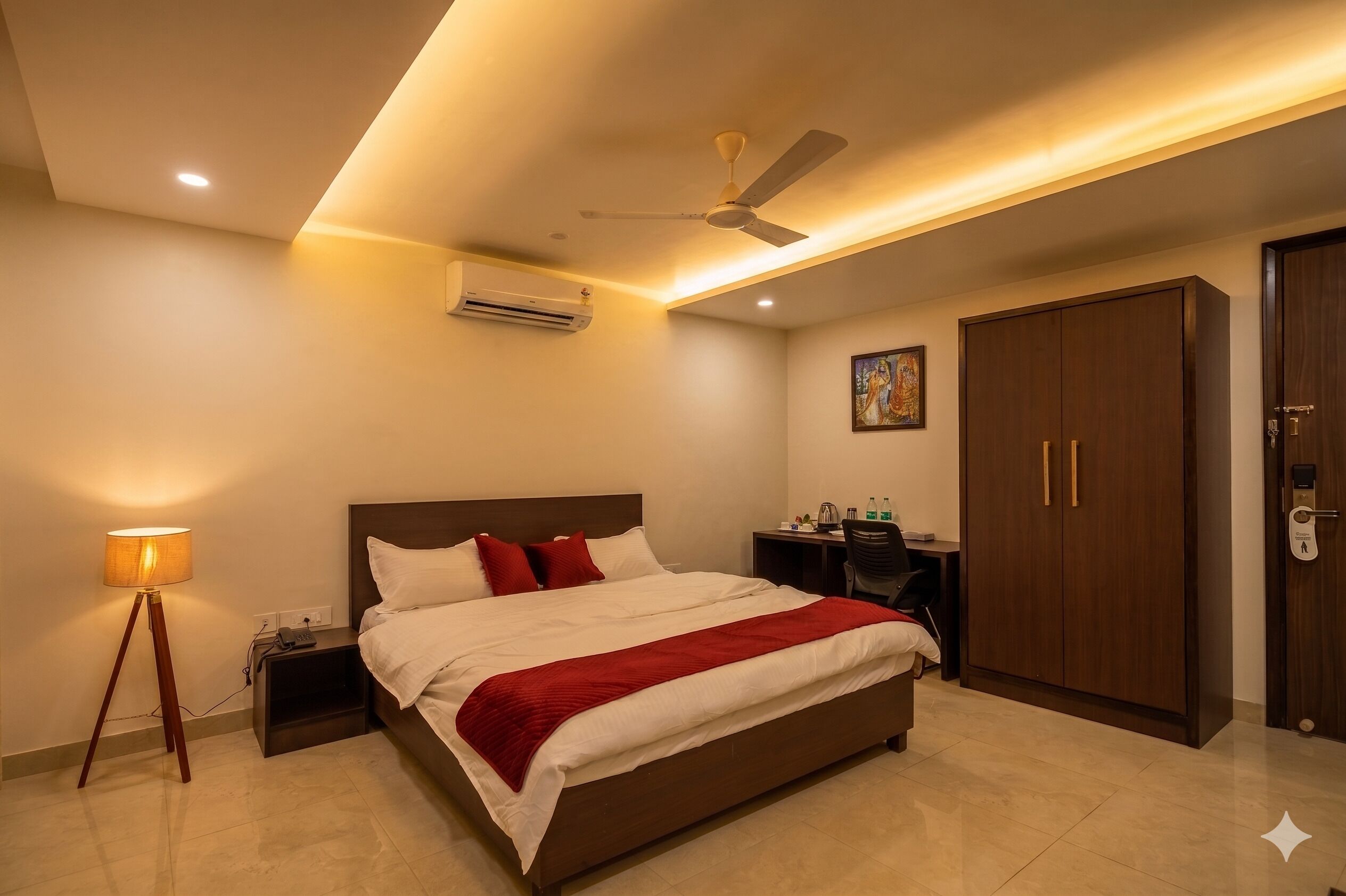 Una habitación de hotel con cama, mesita de noche, lámpara, armario, escritorio y ventilador de techo.