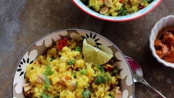 Dos tazones de Poha Upma, uno con una cuña de lima, uno sobre un plato estampado y otro sobre un plato liso.