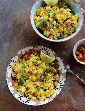 Dos tazones de Poha Upma, uno con una cuña de lima, uno sobre un plato estampado y otro sobre un plato liso.