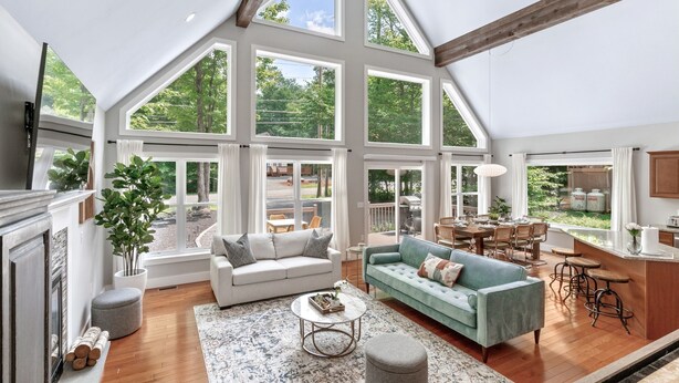 A spacious living room with a high ceiling, large windows, and a cozy seating area.