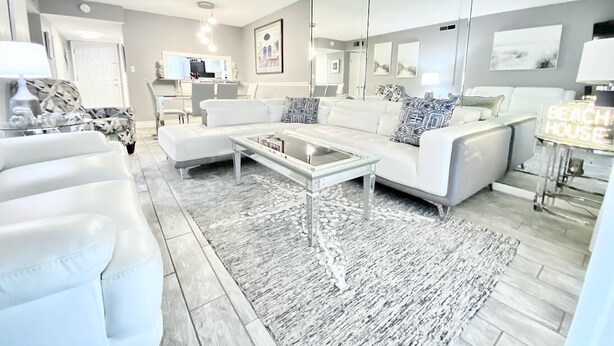 Uma sala de estar moderna com um sofá branco, uma mesa de centro de vidro e um tapete estampado.