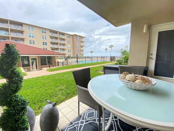 Ein Balkon mit rundem Tisch und Stühlen, Blick auf einen Swimmingpool sowie ein Gebäude mit mehreren Balkonen im Hintergrund.