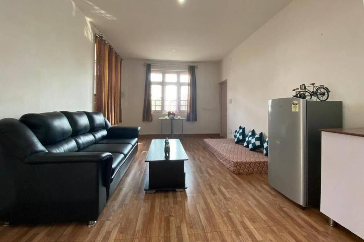 Uma sala de estar com um sofá preto, uma mesa de centro, uma geladeira e uma janela com cortinas.