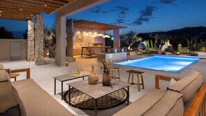 An outdoor patio with a pool, stone pillars, a pergola, and a bar area. - Mirena Luxury Living - Casa di Maria (Αφάντου)