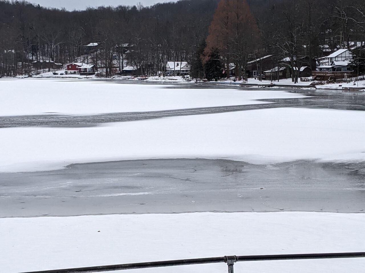 Schneebedeckte Landschaft mit einem zugefrorenen Fluss, Häusern und Bäumen im Hintergrund.