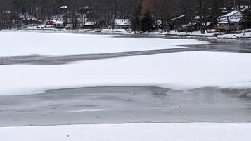Schneebedeckte Landschaft mit einem zugefrorenen Fluss, Häusern und Bäumen im Hintergrund.
