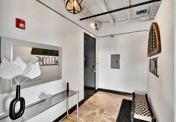 A modern hallway with a mirror, a black door, a small bench, and a patterned rug. - Silos Studio (Waco)