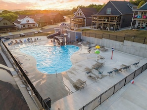 A swimming pool with a water slide, lounge chairs, and umbrellas.