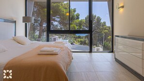 A modern bedroom with a large sliding glass door leading to a balcony, a bed with neatly folded towels, and a minimalist dresser. - Villa ALEX by Abahana Villas (Benissa)