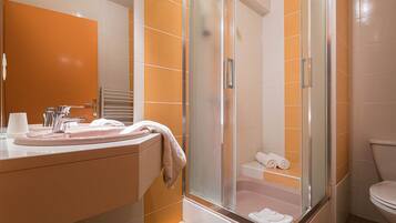 Een badkamer met een douche met glazen wand, een wastafel met spiegel en een toilet.