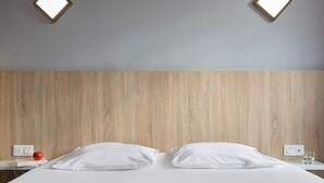 A hotel room with a wooden headboard, two white pillows, a neatly made bed, a red apple, and two bedside tables with glasses of water and a book. - Hotel l'Abri (Blavozy)