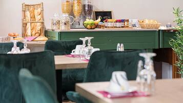 A restaurant interior with green upholstered chairs, a wooden table, and a counter with various food items and condiments.
