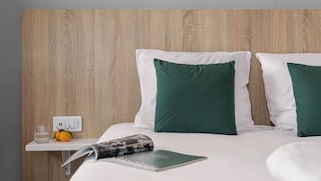 A hotel room with a wooden headboard, white bedding, and a green pillow.