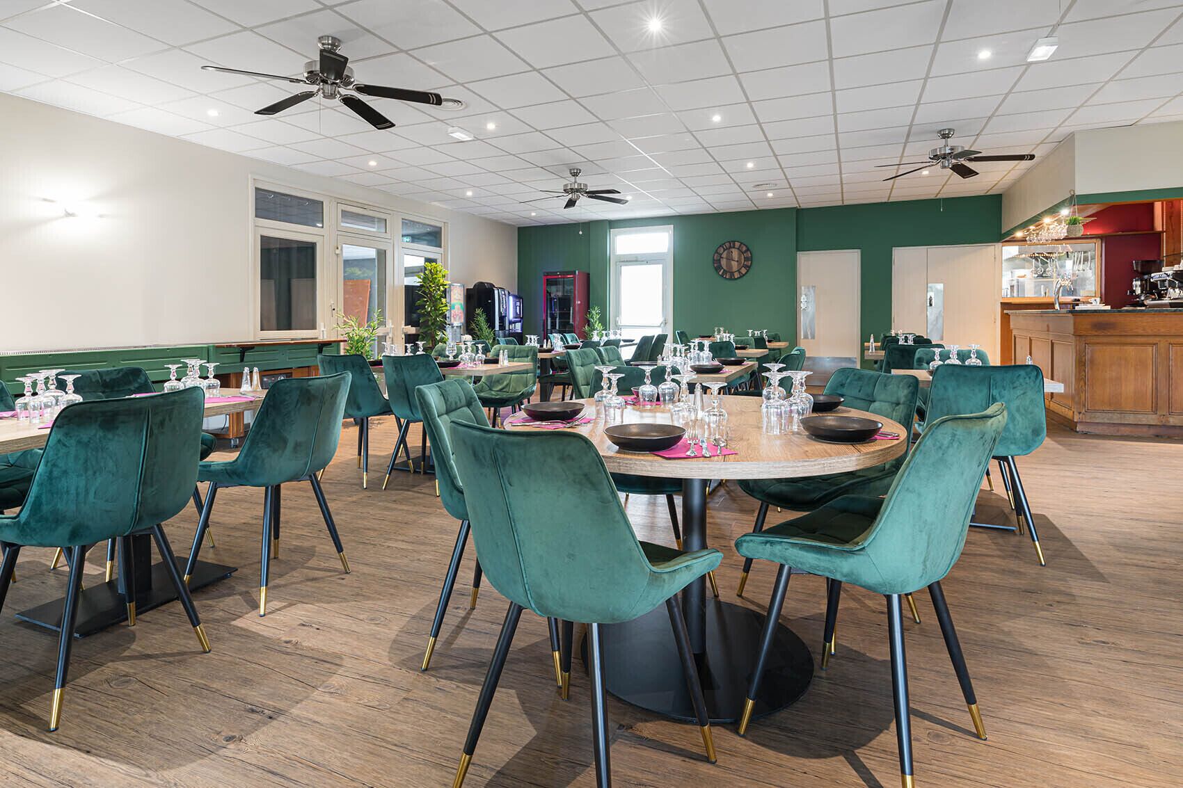A dining area with round tables, teal chairs, and ceiling fans.