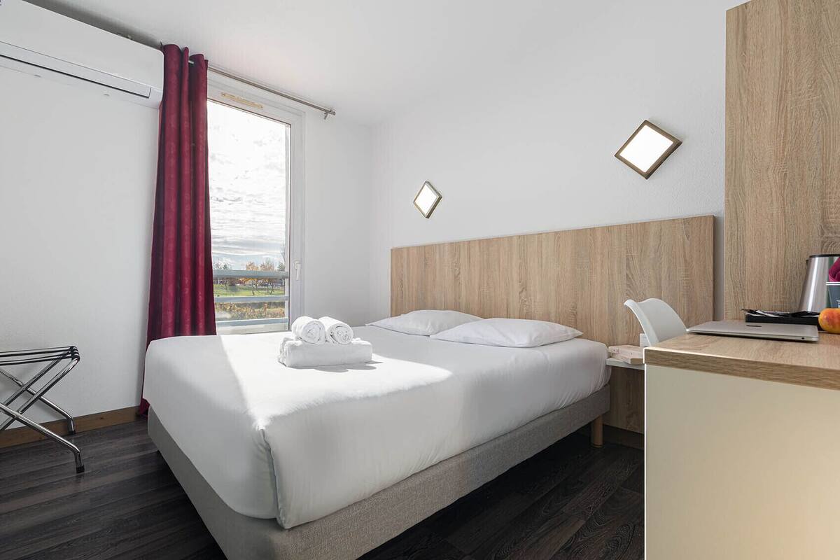 A hotel room with a bed, a desk, and a view of the outdoors.