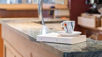 Un comptoir de cuisine avec une tasse de café et un livre, un robinet en acier inoxydable et une fenêtre en arrière-plan.