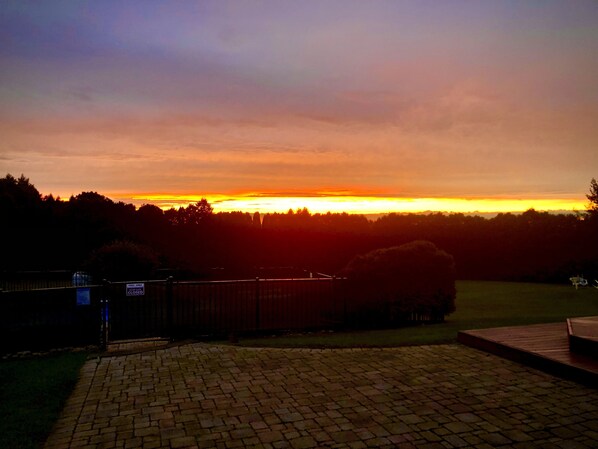 Una vista del atardecer desde un jardín trasero con un patio de ladrillo y una terraza de madera.