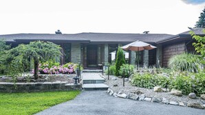 Una casa con un camino de piedra que lleva a una puerta principal, rodeada por un jardín con diversas plantas y flores.