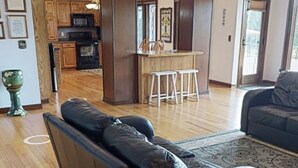 Un salón amplio con un sofá de cuero negro, un comedor con mesa y sillas de madera, y una cocina con armarios de madera y un microondas.