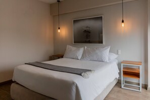A neatly made bed with white linens and a gray throw blanket, a small wooden nightstand, and a wall-mounted light fixture. - w* | High Ceiling and Classy 2BR in Miraflores (Miraflores)