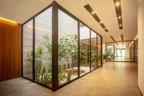 Un pasillo moderno con paredes de vidrio, un panel de madera en un lateral y vistas a un jardín lleno de plantas.
