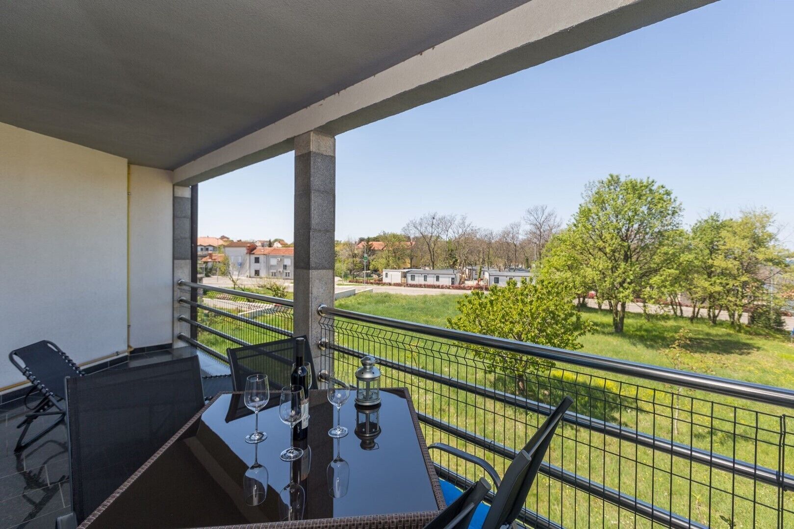 Un balcon avec une table et des chaises, une balustrade et une vue sur un quartier résidentiel avec des maisons et des arbres.