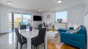 A modern living room with a blue sofa, a white dining table with chairs, and a TV mounted on the wall. - Modern two bedrooms apartment Marea Blue with sea view in Funtana (Funtana)
