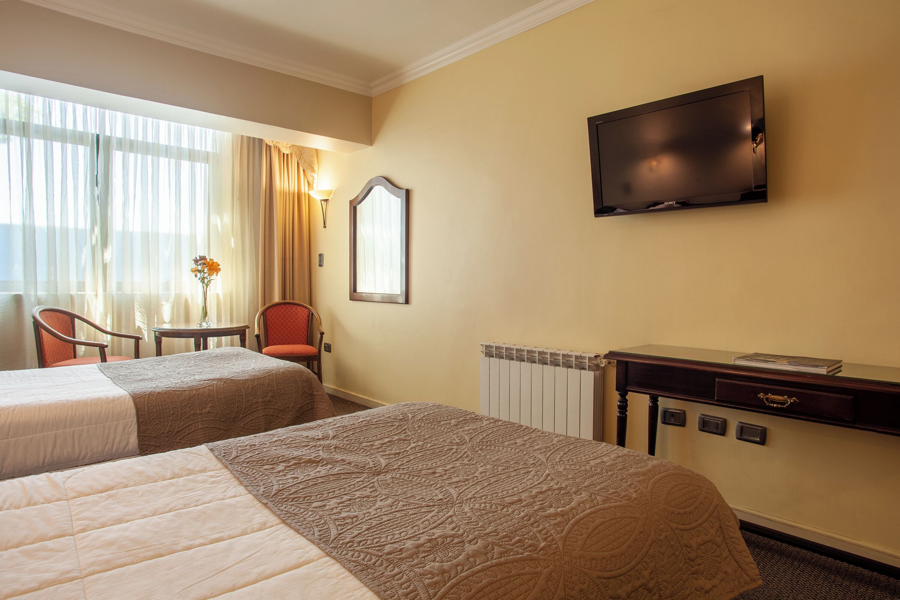 A hotel room with two beds, a TV, a desk, and a chair.