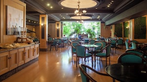 Een ruim restaurant met houten tafels en stoelen, een centrale kroonluchter en uitzicht op groen.