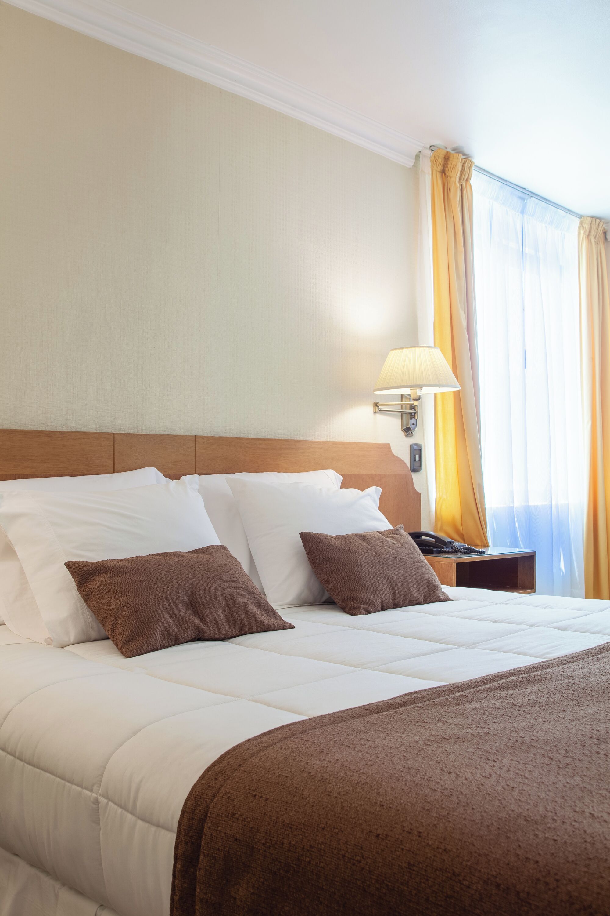 Una habitación de hotel con una cama grande, una mesita de noche con lámpara y un ventanal con cortinas.