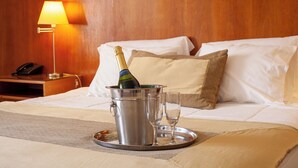 Hotelkamer met een bed, een bedlamp, een minibars kastje, een fles champagne en twee glazen op een dienblad.
