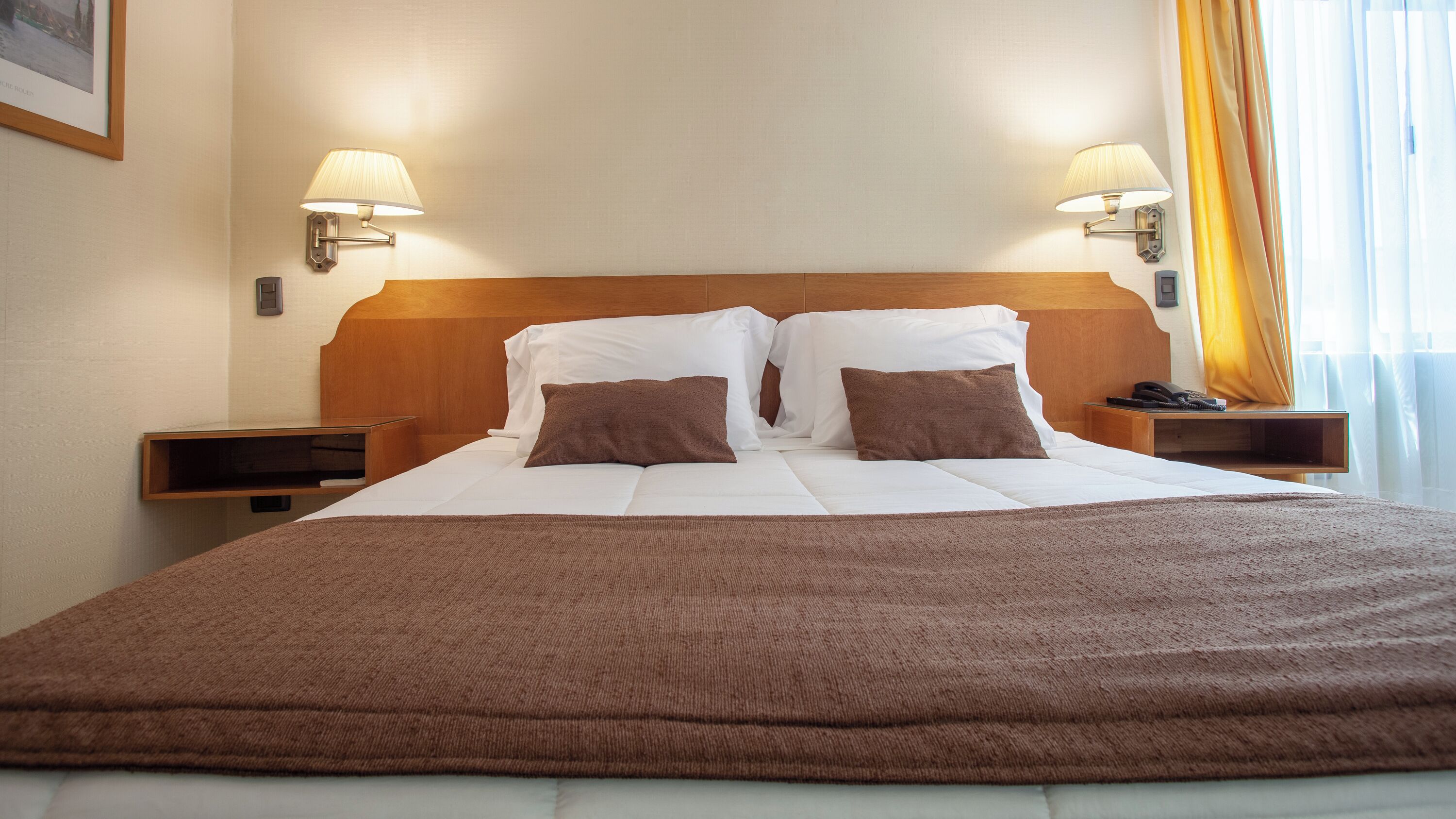 A neatly made bed with white and brown bedding, two bedside tables with lamps, and a wooden headboard.