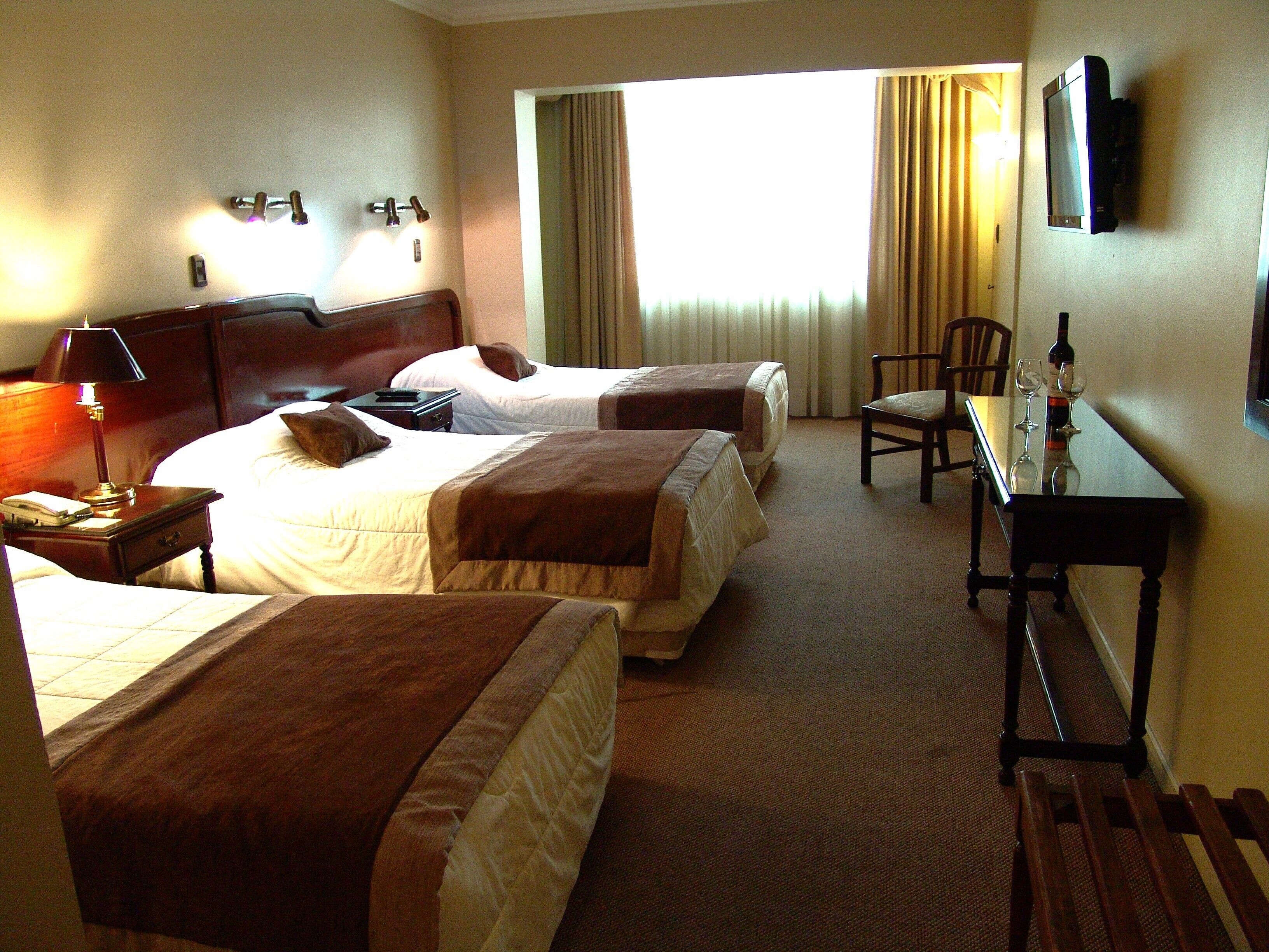 A hotel room with two beds, a desk, a chair, a TV, and a window with curtains.