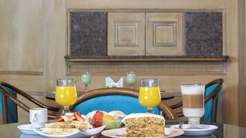 A dining table with breakfast items, two glasses of orange juice, and a cake.