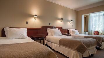 A hotel room with three beds, each with white bedding and a brown throw blanket. There are wall-mounted lamps on either side of the beds.