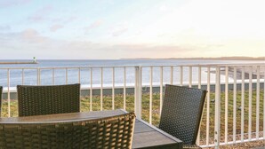 A balcony with wicker chairs and a table overlooking a beach with a lighthouse in the distance. - Promenadenvilla (Lübeck)