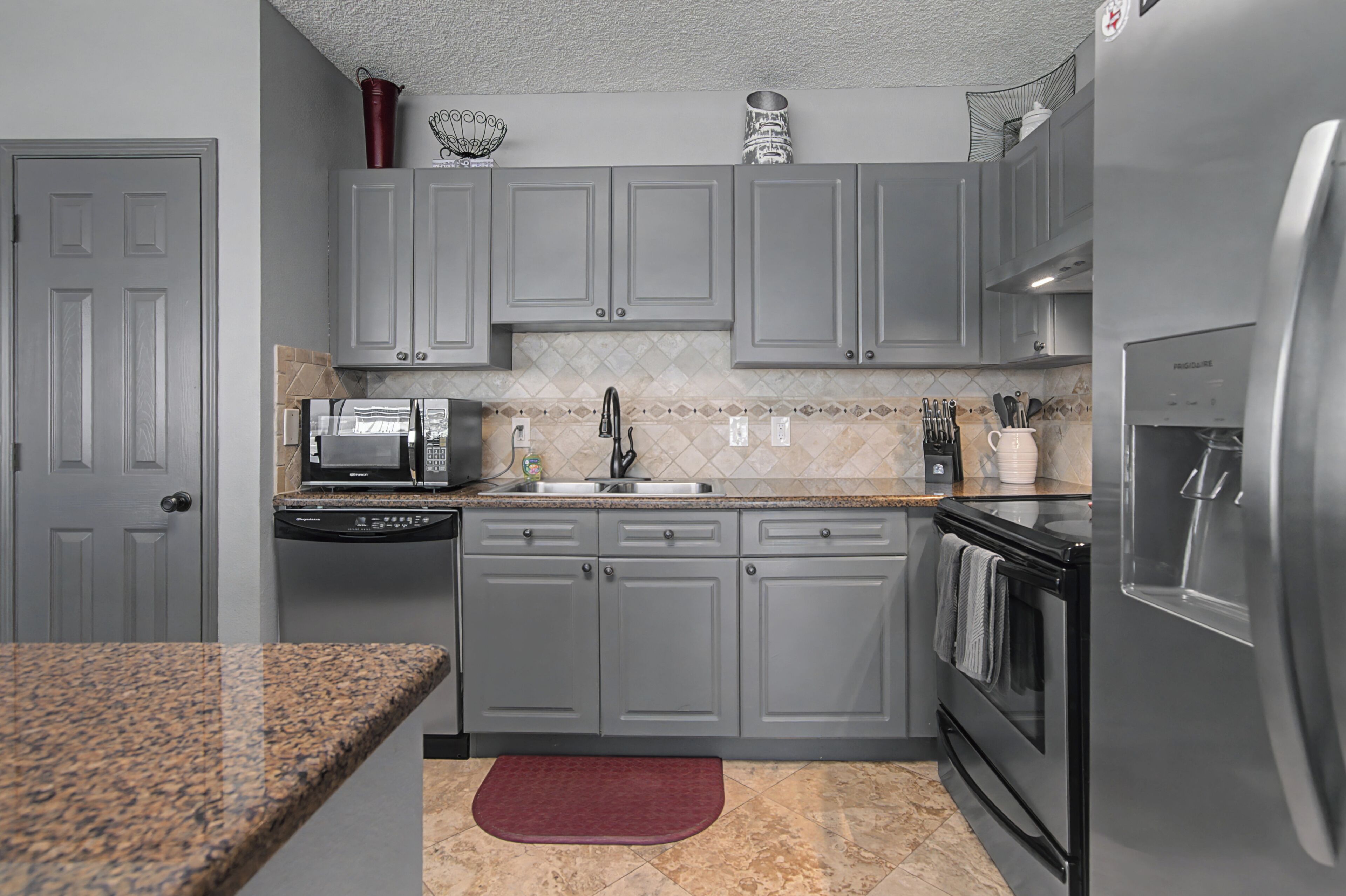 A kitchen with grey cabinets, a microwave, a sink, a dishwasher, and a refrigerator.