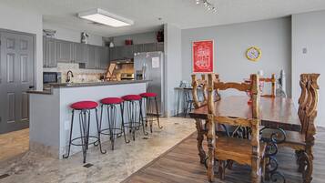 A kitchen with grey cabinets, a central island with stools, a wooden dining table with chairs, and a clock on the wall.