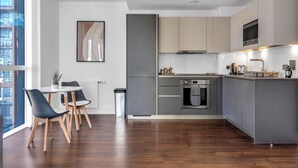 A modern kitchen with grey cabinets, a stainless steel oven, and a dining area with a table and chairs. - Stunning Serviced Apartment-Canary Wharf (London)