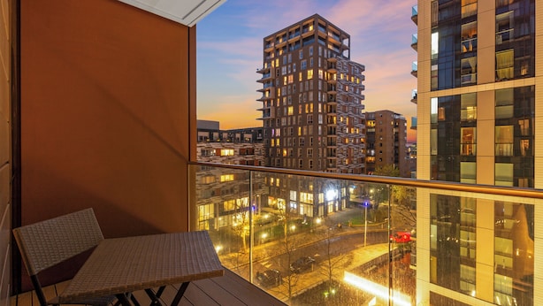 A balcony with a view of a cityscape at dusk, featuring modern buildings and a clear sky. - Stunning Serviced Apartment-Canary Wharf (London)
