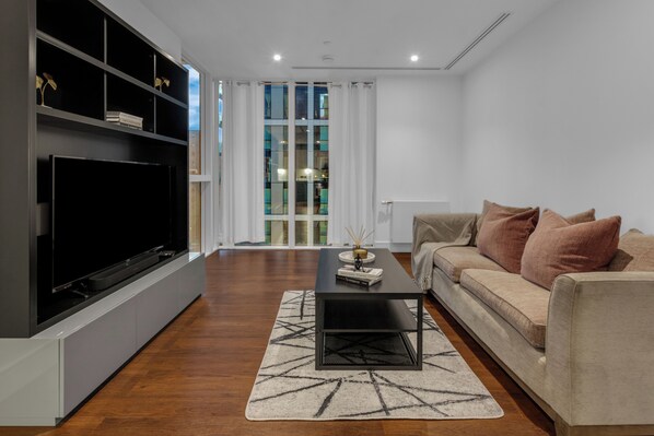 A modern living room with a flat-screen TV, a sofa, a coffee table, and a patterned rug.