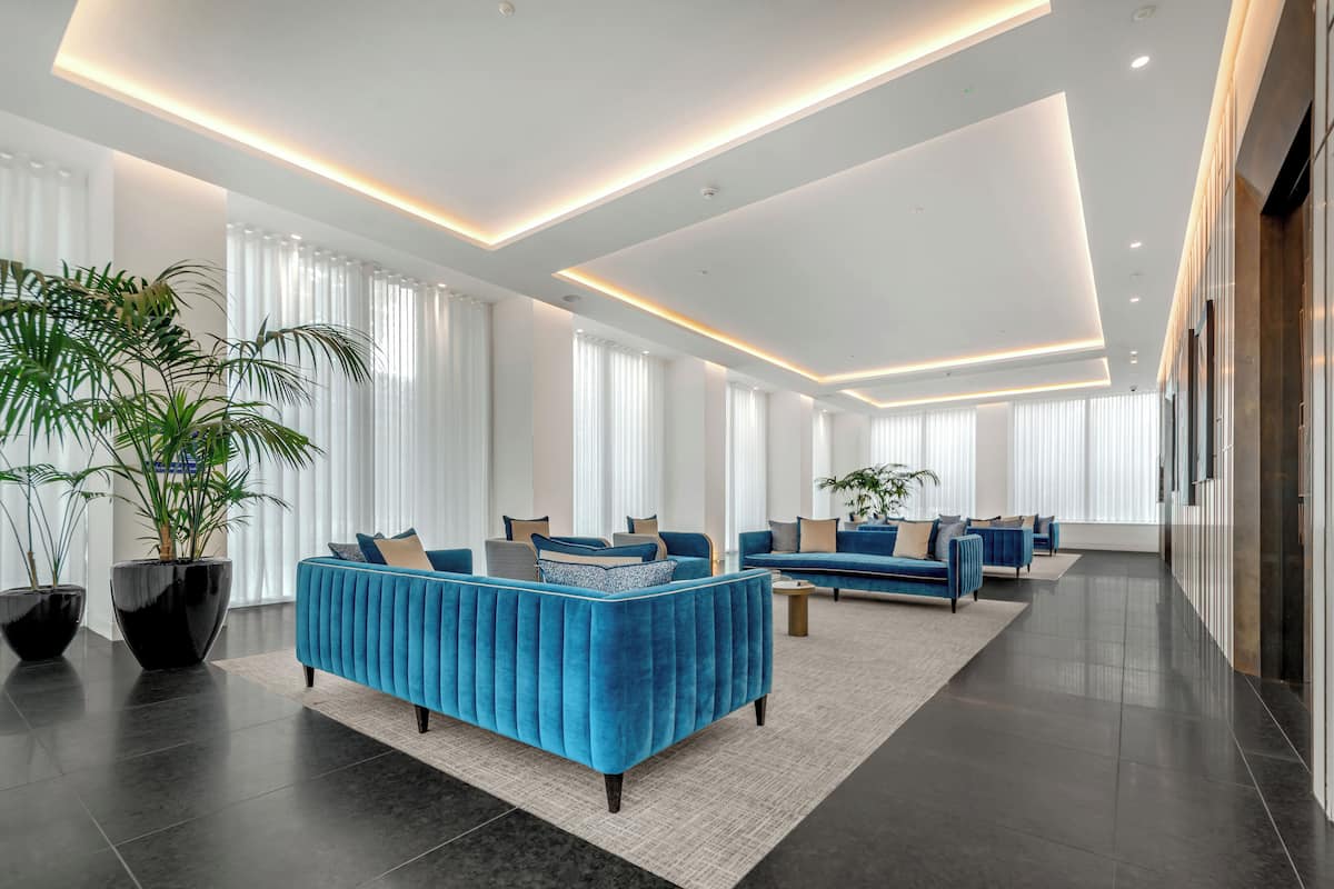 Eine geräumige Lobby mit modernem Design, ausgestattet mit einer großen Sitzgruppe, blauen Sofas und einer üppigen Pflanze.