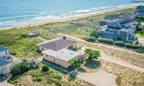 Luchtbeeld van een kustbezit met een groot huis, een kleiner gebouw en een strand op de achtergrond.